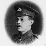 black and white photograph of a First World War soldier with glasses and a moustache. Wearing a cap with the badge of the Queen's Royal West Surrey Regiment.